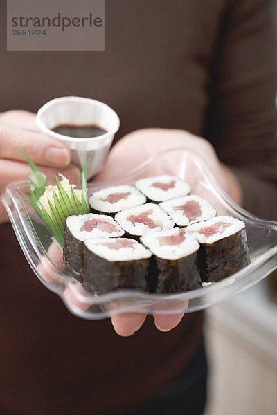 Frau hält Plastikschale mit Maki-Sushi und Sojasauce