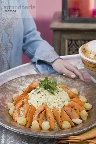 Frau serviert Couscous mit Kürbis  Minze und Zwiebeln
