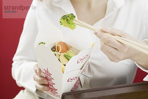 Frau isst asiatisches Gemüsegericht im Take-Out-Behälter