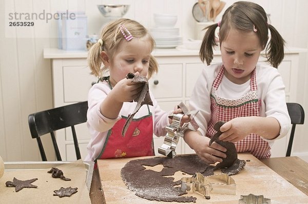 Zwei kleine Mädchen stechen Schokoladenplätzchen aus