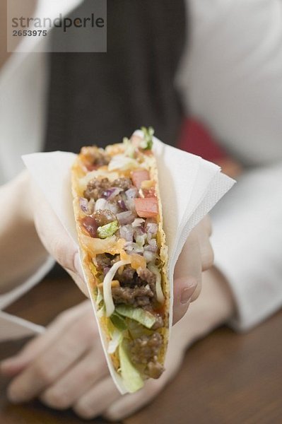 Frau hält Taco mit Hackfleisch in Papierserviette
