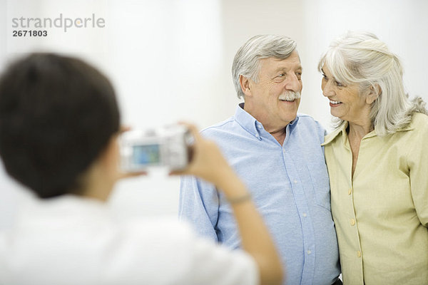 Seniorenpaar wird vom Enkel fotografiert und lächelt sich an.
