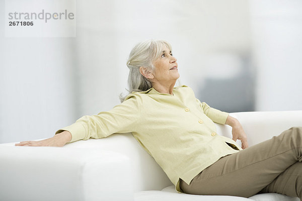 Seniorin auf der Couch sitzend  aufblickend  lächelnd