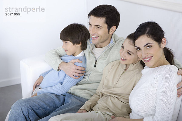 Familie sitzt zusammen auf dem Sofa  schaut weg  Frau lächelt vor der Kamera