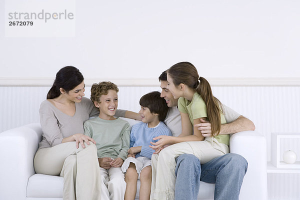Familie mit drei Kindern  die zusammen auf dem Sofa sitzen und reden.
