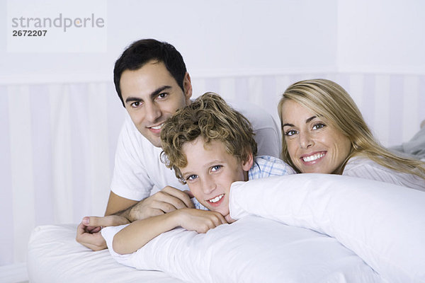 Eltern und Sohn auf dem Bett liegend  lächelnd vor der Kamera  Porträt