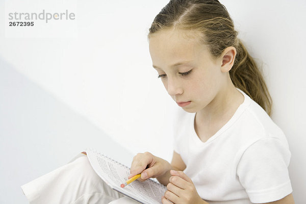 Mädchen lehnt sich an die Wand  liest Notizbuch  hält Bleistift