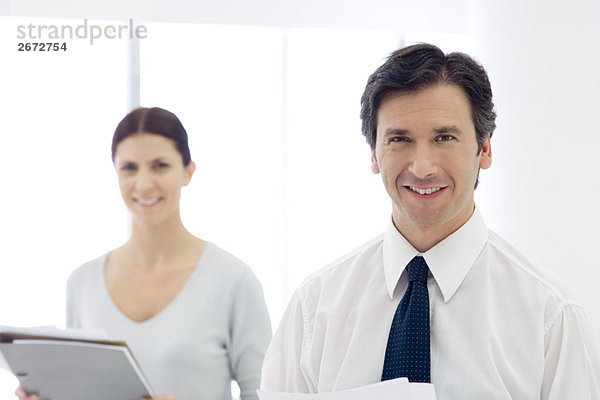 Geschäftskollegen stehend  lächelnd vor der Kamera  Frau hält Dokumente in der Hand