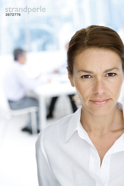 Professionelle Frau mit Blick auf Kamera  Portrait  männliche Kollegen im Hintergrund