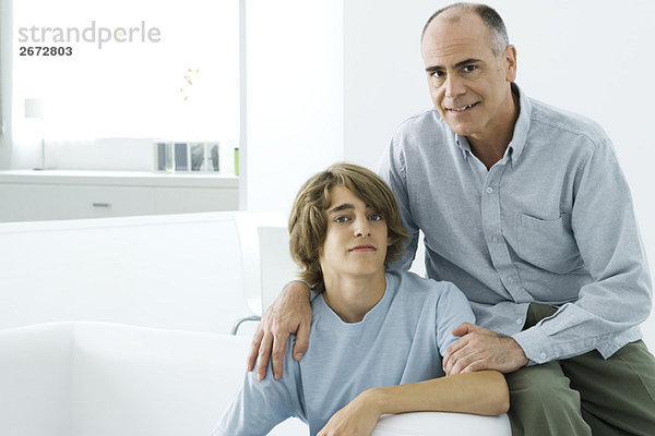 Vater und jugendlicher Sohn sitzen zusammen auf dem Sofa  schauen in die Kamera  Porträt
