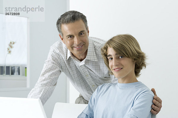Vater und Sohn lächeln vor der Kamera  der Arm des Mannes um die Schulter des Teenagers.