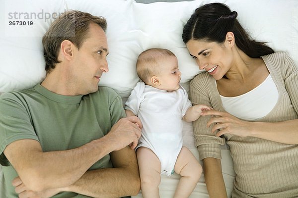 Familie ruht auf dem Bett  Baby liegt zwischen den Eltern  Blick nach oben