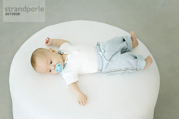 Baby auf dem Hocker liegend  am Schnuller saugend  Hochwinkelansicht