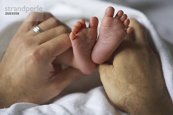 Erwachsen hält Neugeborenen männliches Baby Füße Hände