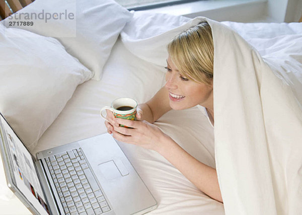Frau bei der Arbeit am Laptop im Bett