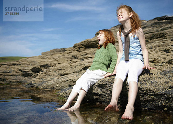 2 Mädchen  die ihre Füße in ein kaltes Felsenbecken stellen.