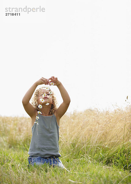 Junges Mädchen macht eine Gänseblümchenkette im Feld