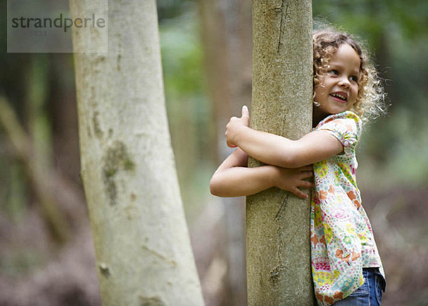 Junges Mädchen umarmt Baum lächelnd