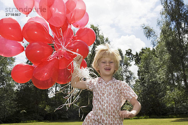 Junge mit einem Haufen roter Luftballons