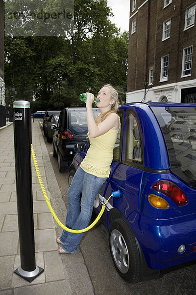 Junge Frau trinkt mit dem Elektroauto
