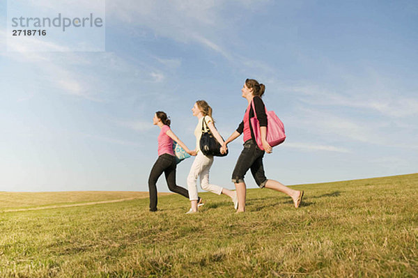 Drei Mädchen  die über einen Grashügel laufen.