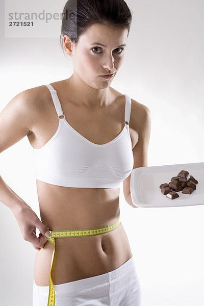 Junge Frau prüft Taille mit Maßband  hält Schokolade auf Tablett