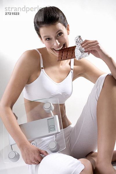 Young woman holding scales  biting into chocolate bar