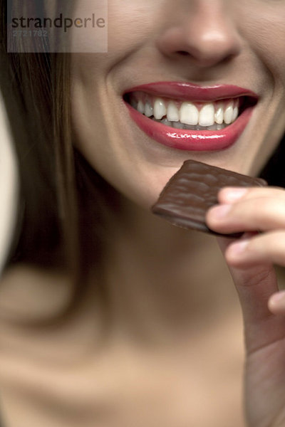Junge Frau  die Schokoladenbonbons in den Mund nimmt  Porträt