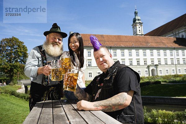 Deutschland  Bayern  Oberbayern  Drei Leute im Biergarten mit Bierkruggläsern  lächelnd