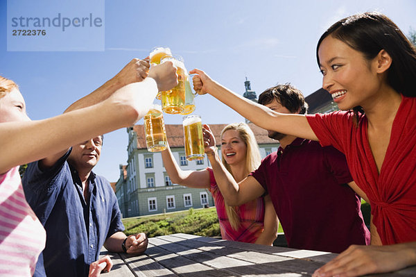 Deutschland  Bayern  Oberbayern  Fröhliche Menschen stoßen sich im Biergarten an.