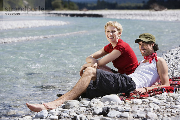Germany  Bavaria  Tölzer Land  Young couple sitting on riverbank