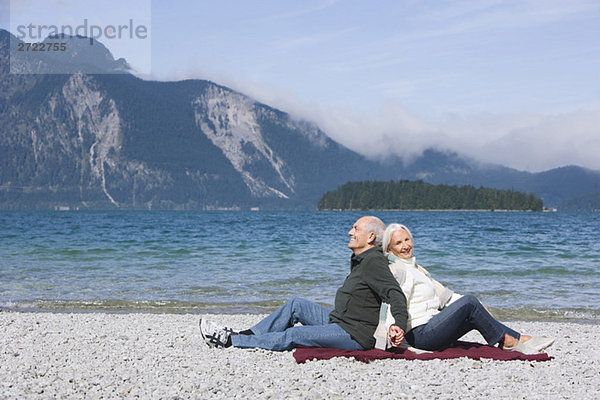 Germany  Bavaria  Senior couple relaxing on lakeshore  sitting back to back