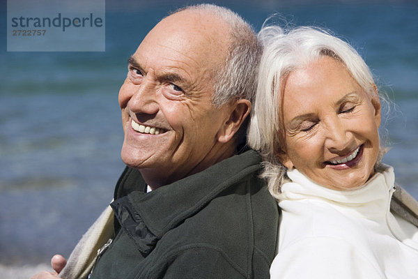 Deutschland  Bayern  Seniorenpaar am Seeufer  Rücken an Rücken  Nahaufnahme  Portrait