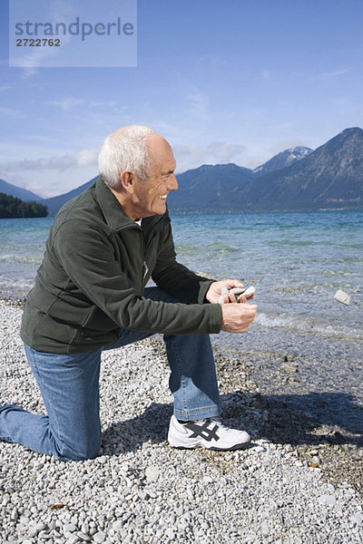 Senior man on lakeshore  about to skimming a stone
