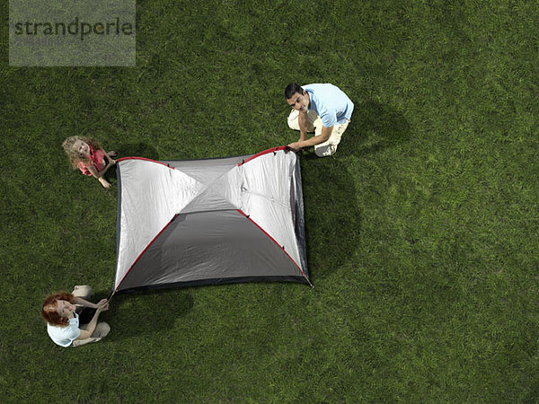 Eine Familie baut ein Zelt auf Rasen auf.