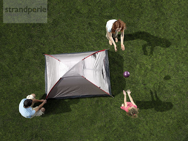 Eine junge Familie baut ein Zelt auf und spielt mit einem Ball.