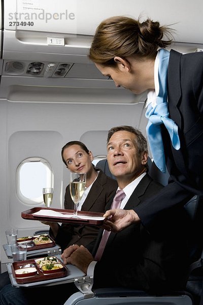 Geschäftsleute in einem Flugzeug  die Mahlzeiten und Champagner bekommen.