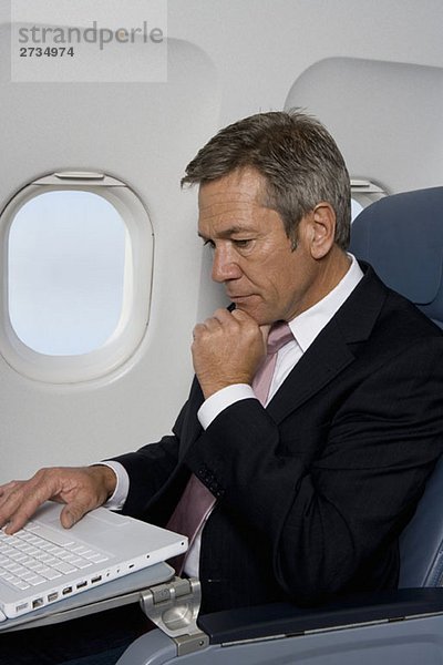 Ein Geschäftsmann  der einen Laptop in einem Flugzeug benutzt.