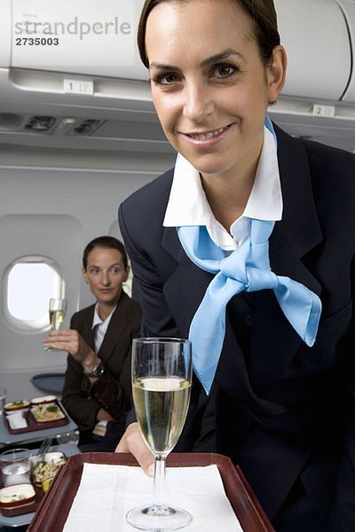 Eine Flugbegleiterin  die Champagner serviert.