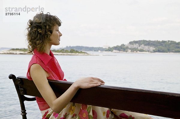 Eine Frau  die auf einer Bank sitzt und auf das Meer schaut.