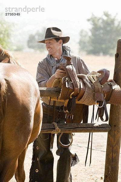 Ein Rancher  der einen Pferdesattel auf einem Zaun vorbereitet.