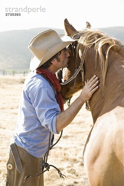 Ein Cowboy  der ein Pferd küsst.