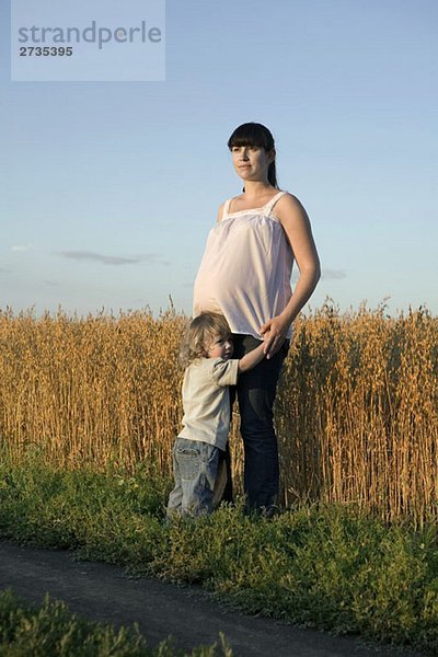 Eine schwangere Frau und ihr kleiner Junge stehen in der Nähe eines Weizenfeldes.