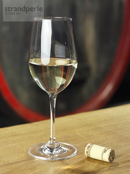 Ein Glas Weißwein mit einem Korken daneben  Stilleben