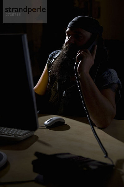 Ein Biker sitzt in einem abgedunkelten Büro am Telefon.