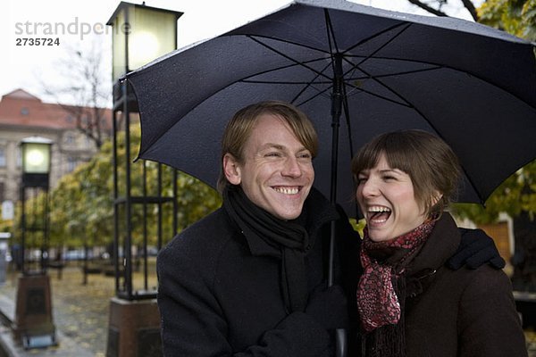 Junges Paar lacht unter einem Regenschirm