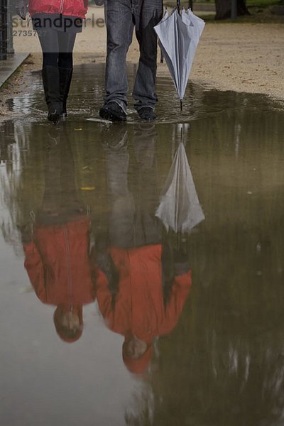 Pfütze mit dem Spiegelbild eines jungen Paares beim Gehen