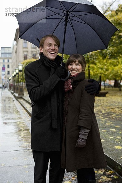 Junges Paar steht und hält Regenschirme