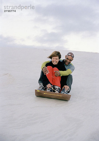 Ein Mann und eine Frau rutschen eine Sanddüne hinunter.
