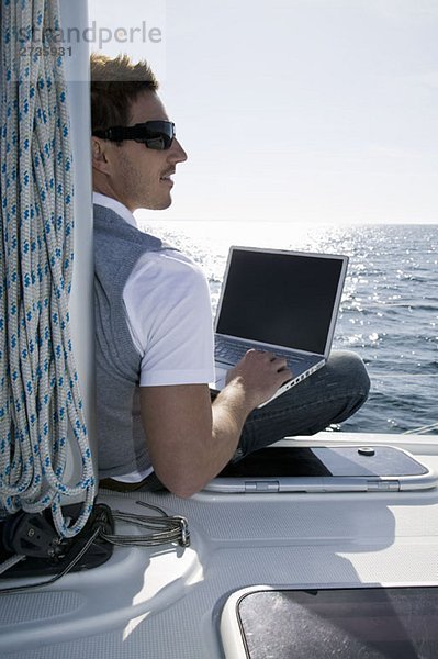 Rückansicht eines Mannes mit einem Laptop auf einer Yacht